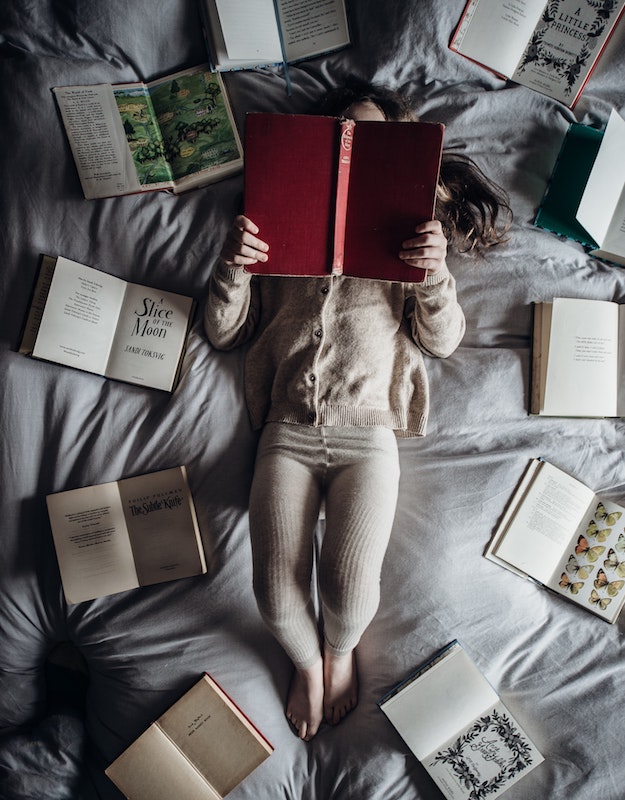 child laying on bed surrounded by books