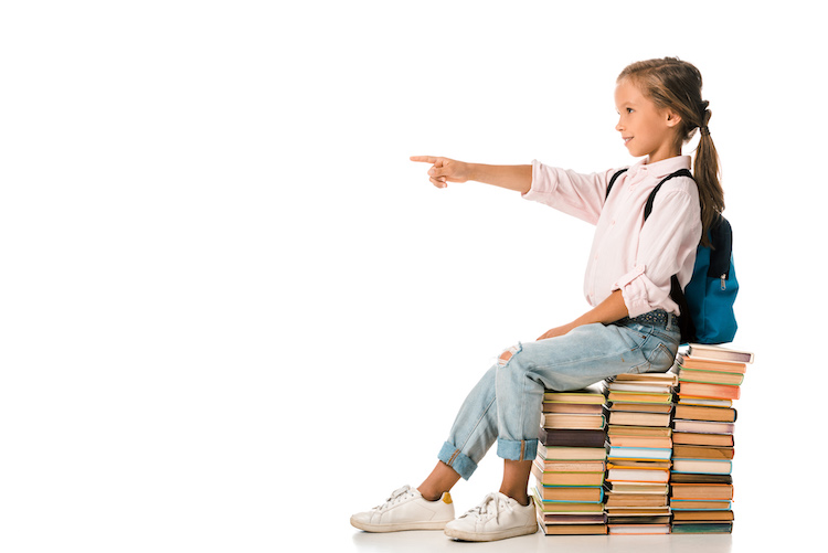cheerful kid sitting on books and pointing with finger on white