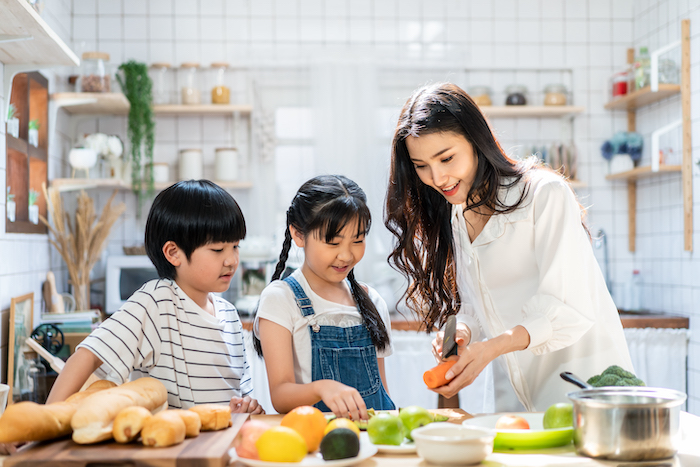 Lovely cute Asian family playing, making food in kitchen at home. Portrait of smiling mother and children standing at cooking counter that food ingredient put on table. Happy family activity together.